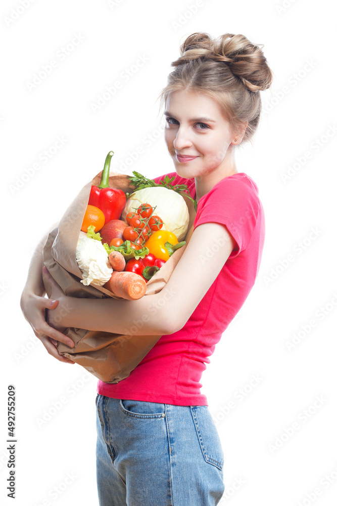 Vegan Healthy Lifestyle. Caucasian Blond Girl Holding Eco Paper Bag with Vegetables and Groceries In Casual Clothing On White Background Vegan Healthy Lifestyle. Caucasian Blond Girl Holding Eco Paper Bag with Vegetables and Groceries In Casual Clothing On White Background