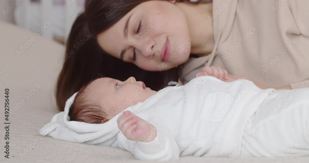 A mother leans over her newborn baby lying on the bed A mother leans over her newborn baby lying on the bed