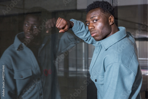 Attentive young black male standing near glass wall and looking at camera
