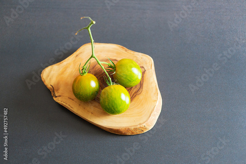 Green zebra tomatoes on olive wood plate on black background