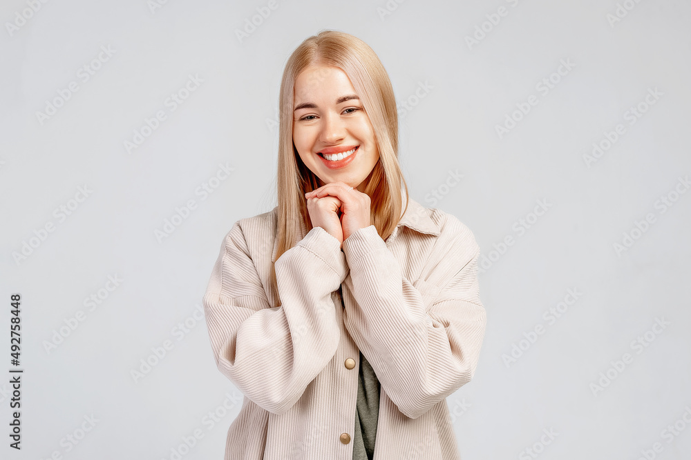 Lovely girl makes gratitude gesture presses palms to chin feels touched pleased by compliments says thank you expresses thankfullness, gray background. Body language and real feelings concept Lovely girl makes gratitude gesture presses palms to chin feels touched pleased by compliments says thank you expresses thankfullness, gray background. Body language and real feelings concept