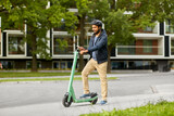 transport, technology and people and concept - happy smiling young man in helmet with electric scooter using smartphone on city street