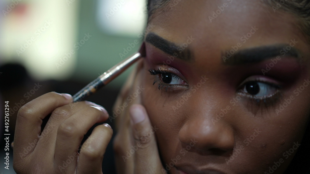 Obraz premium A young black girl applying make-up in front of mirror