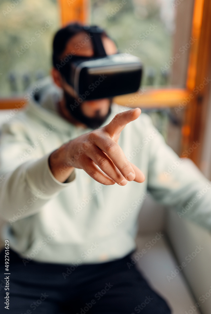 Selective focus at hand making gesture in air, virtual reality. Young man wearing VR goggles while playing