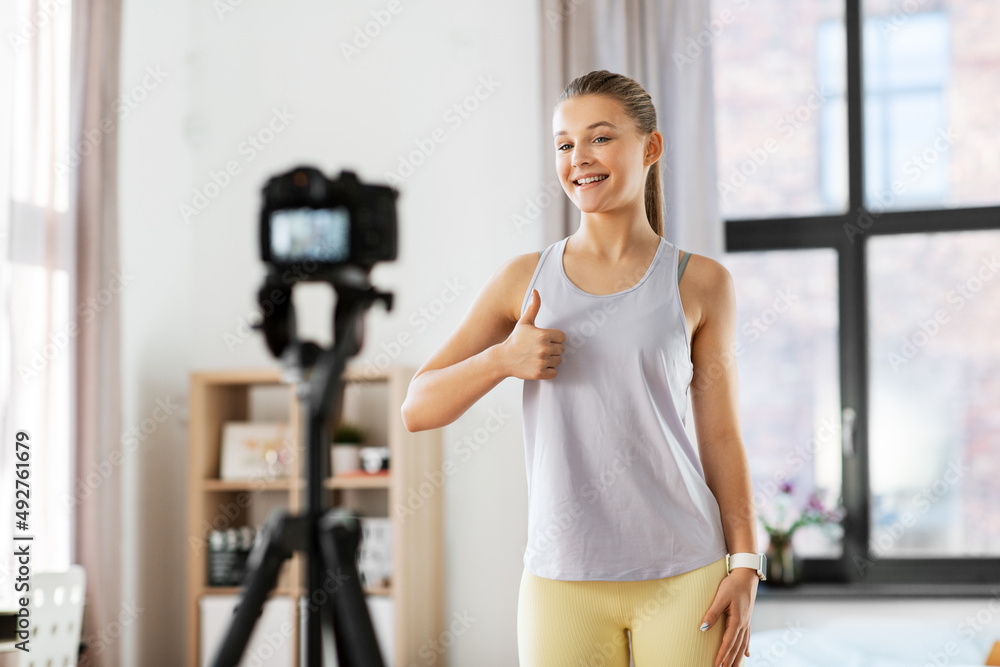 fitness, sport and video blogging concept - happy smiling teenage girl or blogger with camera on tripod recording online gym class at home and showing thumbs up fitness, sport and video blogging concept - happy smiling teenage girl or blogger with camera on tripod recording online gym class at home and showing thumbs up