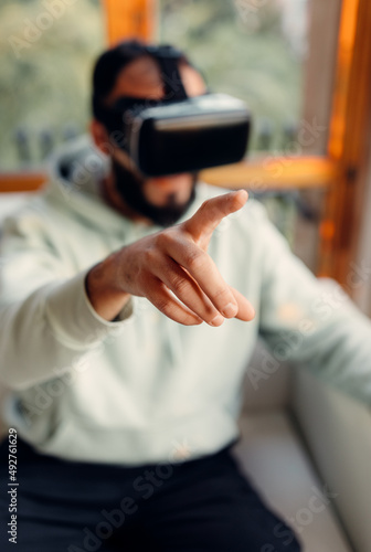 Selective focus at hand making gesture in air  virtual reality. Young man wearing VR goggles while playing