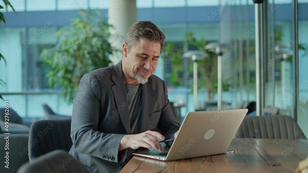 Happy middle age businessman using laptop computer in office. Older casual man working online on terrace of cafe, smiling. Happy middle age businessman using laptop computer in office. Older casual man working online on terrace of cafe, smiling.