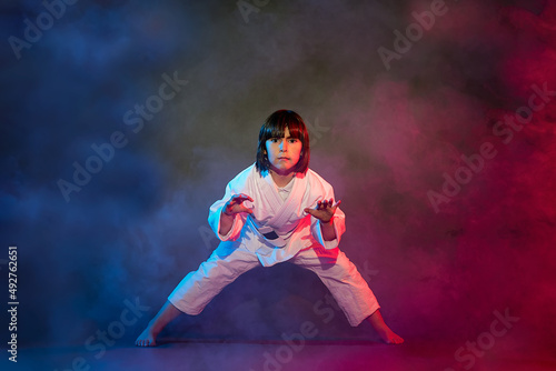 5-year-old elementary school girl, in kimono, practicing martial arts among smoke and colored lights.