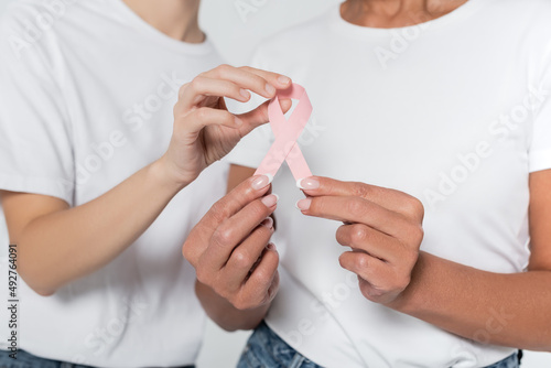 Cropped view of women holding ribbon of breast cancer awareness isolated on grey.