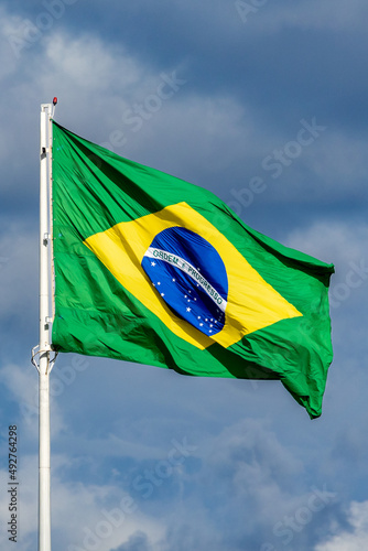 The Brazilian flag fluttering on the pole. Blue sky.