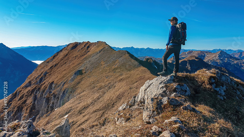 A man standing on a rock and enjoying the panoramic view near mount Eisenerzer Reichenstein in Styria,Austria,Europe.The mountain ridges are part of the Ennstal Alps.Hiking trail,Wanderlust.Sunny day.