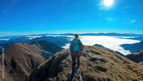 Woman with backpack hiking and admiring a scenic view from mount Eisenerzer Reichenstein in Styria, Austria, Europe. Ennstal valley is covered in clouds. Hiking trail, Wanderlust. Freedom concept photo