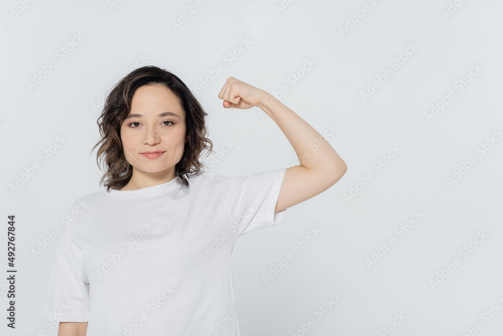 Young woman in white t-shirt showing muscles isolated on grey. Young woman in white t-shirt showing muscles isolated on grey.