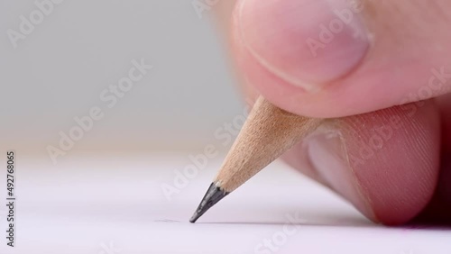Macro of pencil writing or drawing. Unknown person drawing line or letter on white paper.