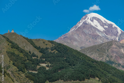 Distant view on Gergeti Trinity Church in Stepansminda, Georgia. The church is located the Greater Caucasian Mountain Range. Clear sky above the snow-capped Mount Kazbegi in the back. Hiking trail
