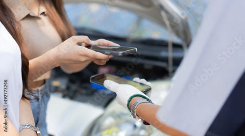 Asian women get contact numbers from Asian male auto mechanics after fixing the car engine problem and QR code scan to pay for fixing vehicle service. Car repair, and maintenance concept.