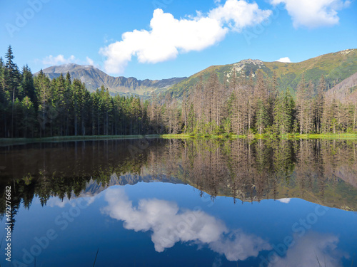 A panoramic view on Smreczynski Staw in Tatra Mountains in Poland. Glacial tarn at the mouth of Pysznianska Valley. The high Tatra chains are reflecting in the calm surface of the lake. White clouds