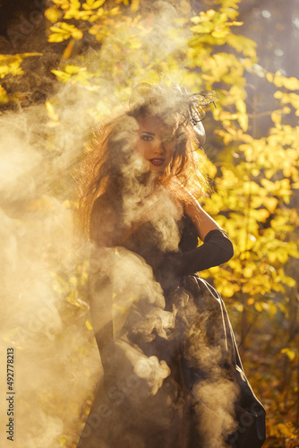 young girl in a long black widow's dress, in the autumn more often woods covered with smoke
