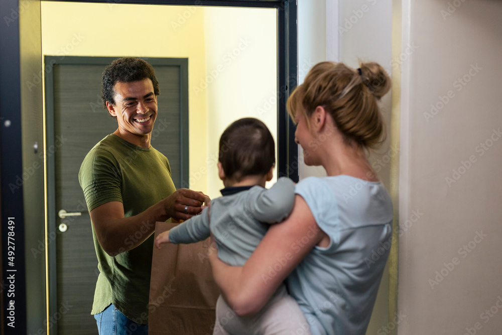 Obraz premium Delivery man delivers package to a mother with a baby in her arms.