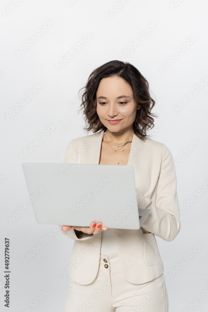 Businesswoman using laptop while standing isolated on grey. Businesswoman using laptop while standing isolated on grey.