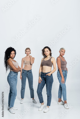 Full length of multiethnic friends in jeans and tops posing on grey background.