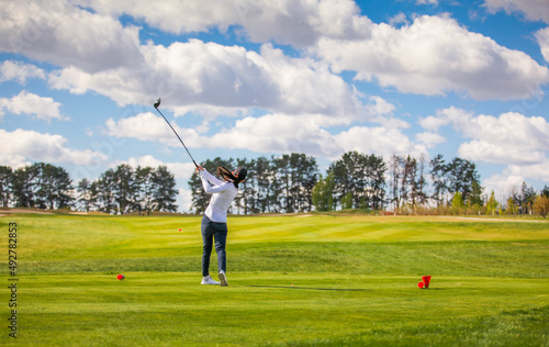 Woman golf player teeing off the ball, view from behind. Space for text. Sport playground for golf concept - wide landscape as background for your lettering about golf playing. Royal sport.