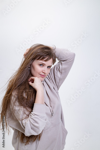 portrait of a pretty blonde girl with long hair in a beige hoodie on a light background