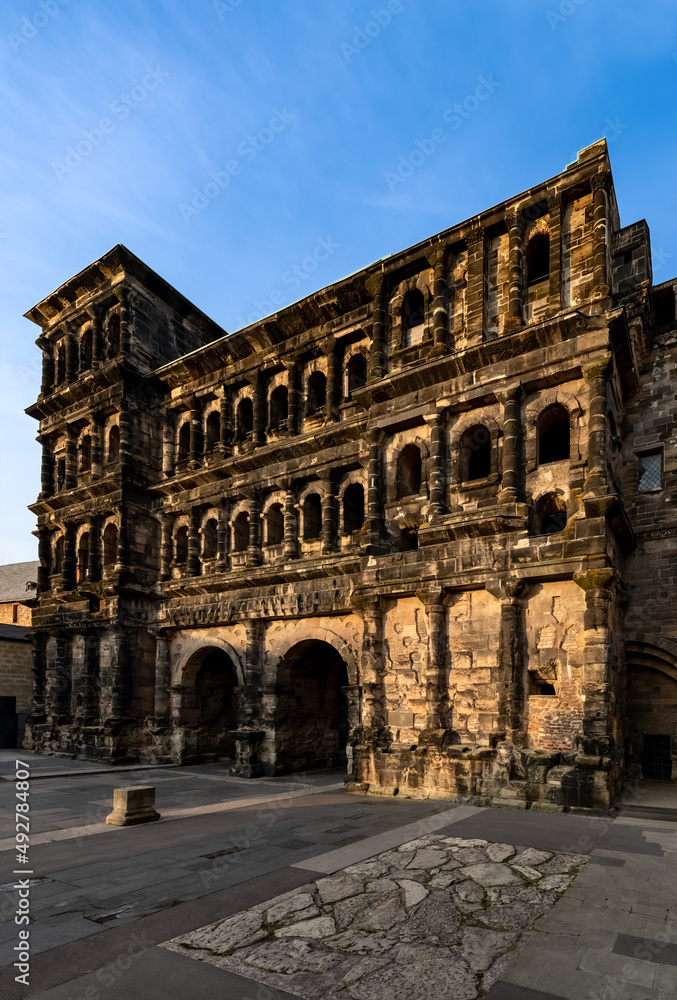 The “Porta Nigra“ (Latin black gate) is a large Roman city gate in Trier, Germany. Largest Roman city gate north of the Alps. Historic landmark monument sight in town centre with warm evening light.