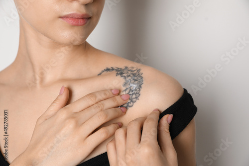 Woman applying cream onto tattoo on her skin against light background, closeup