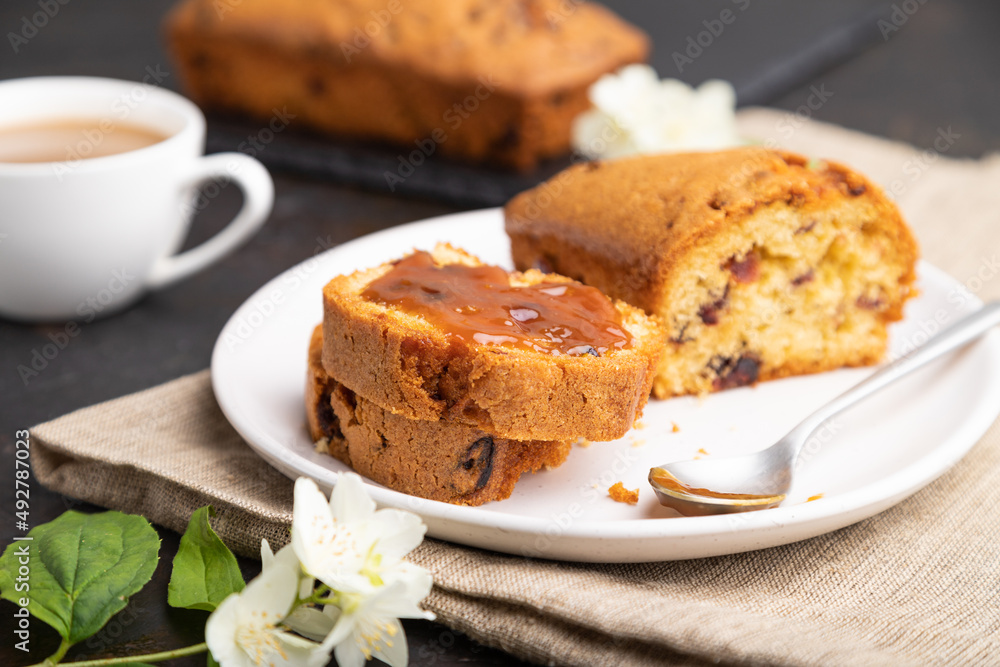 Homemade cake with raisins, almonds, soft caramel and a cup of coffee on a black concrete background. Side view, selective focus. Homemade cake with raisins, almonds, soft caramel and a cup of coffee on a black concrete background. Side view, selective focus.