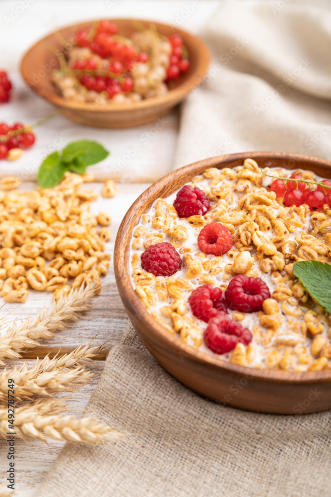 Wheat flakes porridge with milk, raspberry and currant in wooden bowl on white wooden background. Side view, selective focus. Wheat flakes porridge with milk, raspberry and currant in wooden bowl on white wooden background. Side view, selective focus.