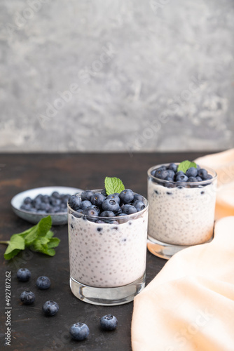 Yogurt with blueberry and chia in glass on black concrete background. Side view, copy space.