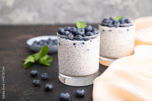 Yogurt with blueberry and chia in glass on black concrete background. Side view, close up.