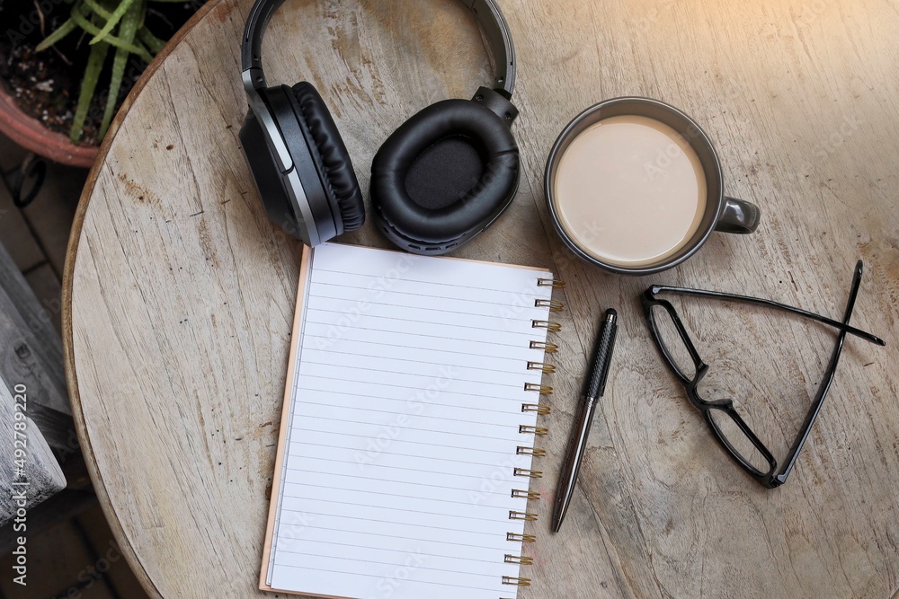 Open notebook with empty pages with pen, eyeglasses, a cup of coffee, and headphones. Top view, flat lay. Open notebook with empty pages with pen, eyeglasses, a cup of coffee, and headphones. Top view, flat lay.