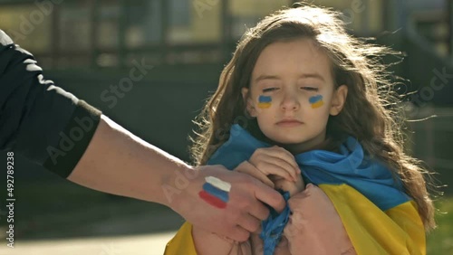 Man's hand with the image of the Russian flag roughly pulls the hand of a little girl with the Ukrainian flag. Russia's perfidious attack on Ukraine.