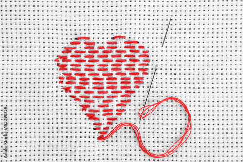 Canvas with embroidered heart and needle as background, top view photo