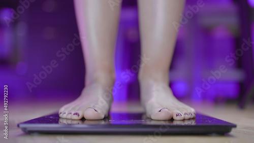 Female feet step on scale to measure weight with purple background