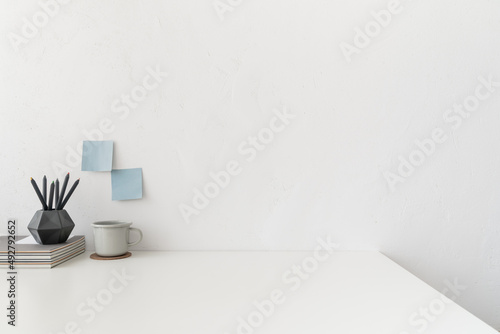 Close up of creative office table mock up with metal mug, office supplies and white wall copy space..