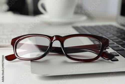 Modern laptop and glasses on white table, closeup