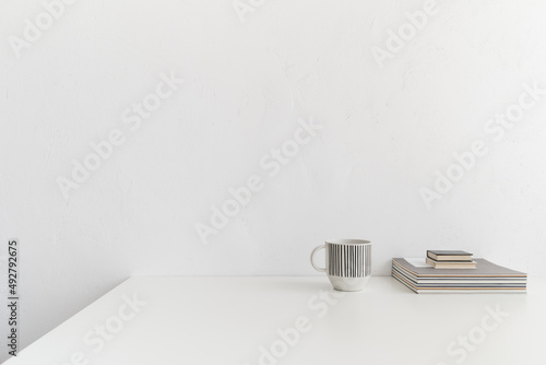 Front view white desk with books and coffee mug and white wall copy space..