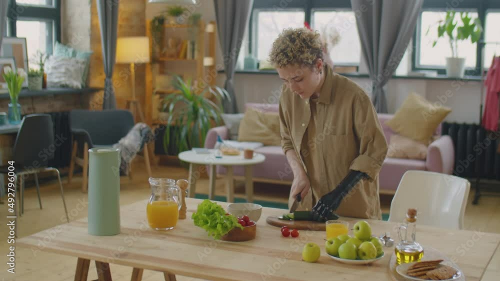 Girl with prosthetic arm cutting fresh vegetables at kitchen table while cooking salad at home Girl with prosthetic arm cutting fresh vegetables at kitchen table while cooking salad at home