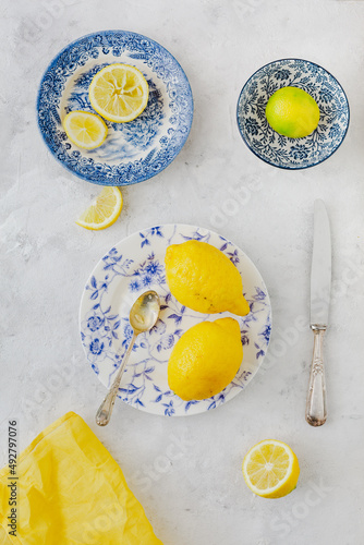 Vintage plates with yellow and green citrus next to old knife and spoon on white background and yellow napkin