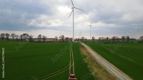 Wind farm among greenery with trees on a cloudy day with a car driving towards the windmill recorded from a drone in a wide shot photo