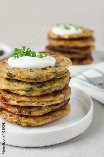 Delicious zucchini pancakes with sour cream served on light grey table, closeup