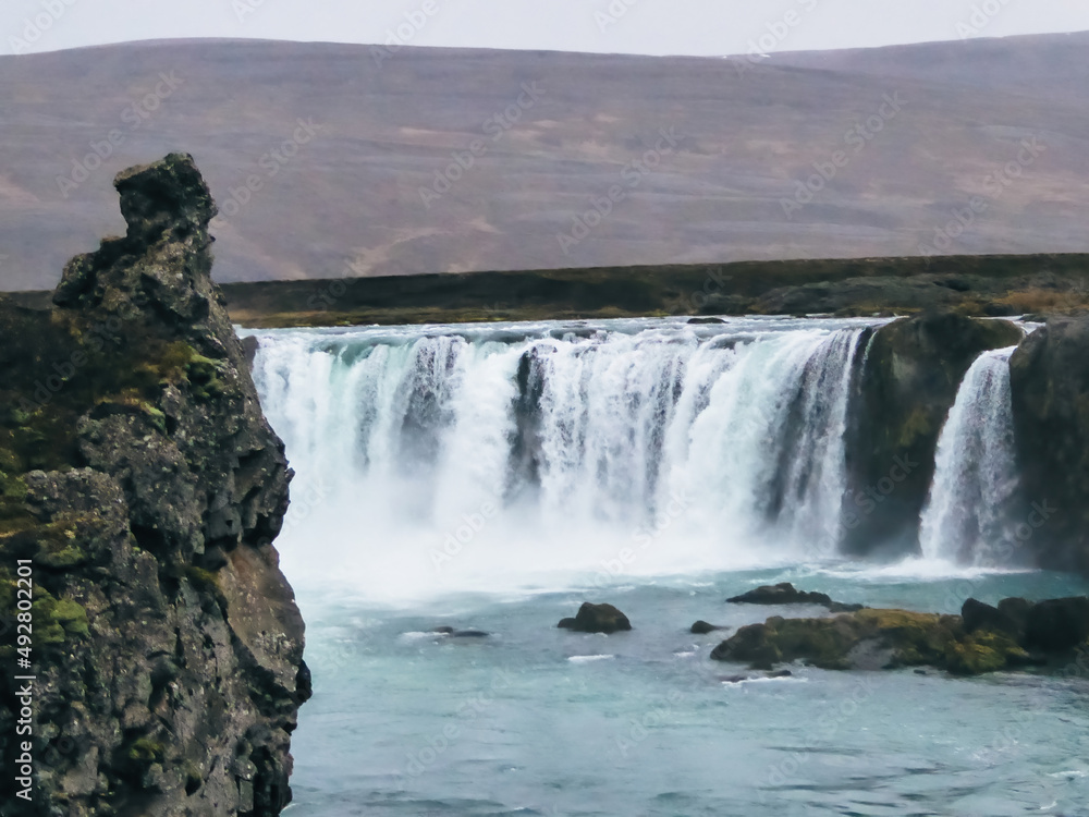 A immense waterfall, surrounded by mountains. Edgy rock formation in the foreground. Stones overgrown with moss. Calm water. Mist sprinkling around the waterfall. Powerful force of nature. A immense waterfall, surrounded by mountains. Edgy rock formation in the foreground. Stones overgrown with moss. Calm water. Mist sprinkling around the waterfall. Powerful force of nature.