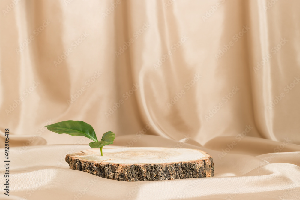 Empty wooden podium with bark and green leaf on satin beige textile, natural tree display for product presentation Empty wooden podium with bark and green leaf on satin beige textile, natural tree display for product presentation