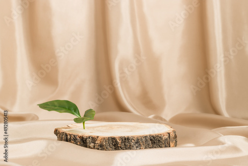 Empty wooden podium with bark and green leaf on satin beige textile, natural tree display for product presentation