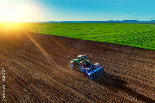 Farmer with tractor seeding crops at field photo