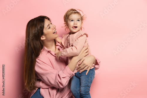 Play. Portrait of young woman and little girl, mother and daughter isolated on pink studio background. Mother's Day celebration. Concept of family, childhood, motherhood