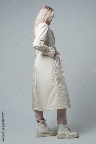 attractive woman in white coat and trousers looking at camera on grey background
